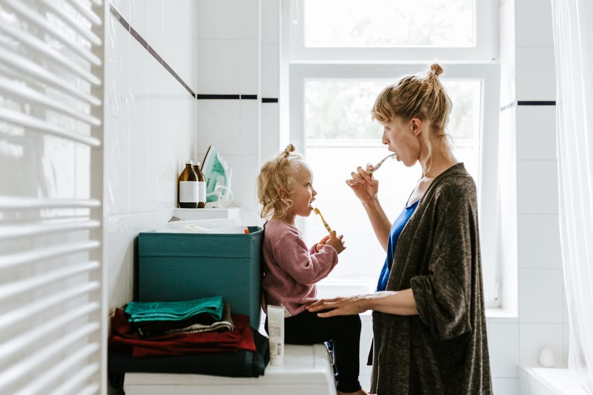 A parent and young child brushing their teeth together at home