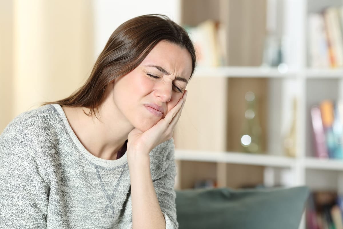 A patient wincing and holding their jaw from TMJ discomfort