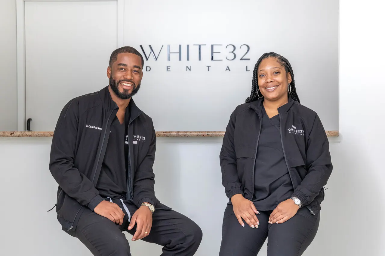 Dr. Charles White and a White32 Dental team member seated beneath the practice sign in the reception area